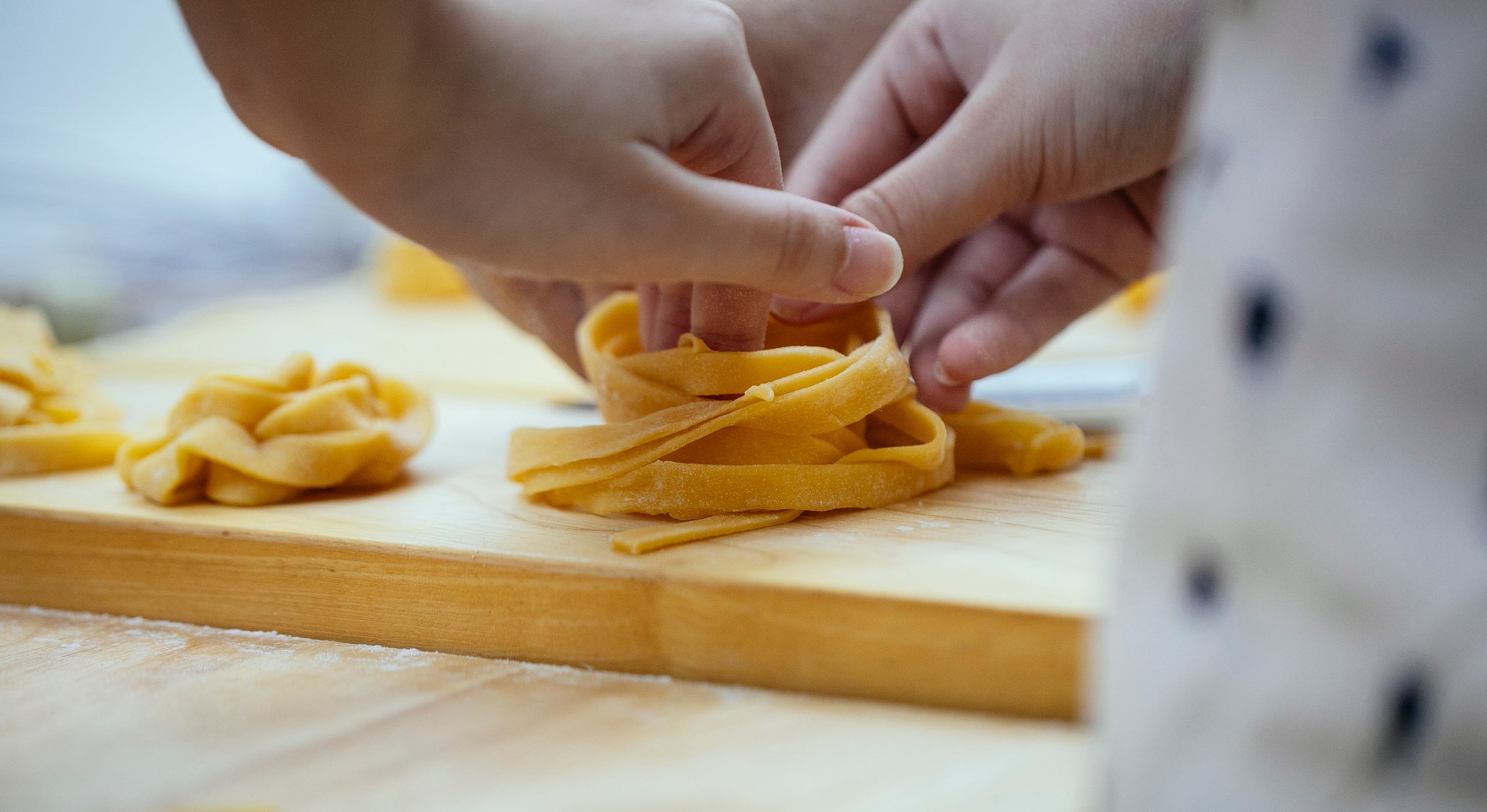Home Hände legen frische Tagliatelle auf ein Holzbrett